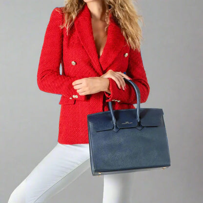 Woman wearing red tweed blazer with gold buttons and holding a navy synthetic leather tote bag