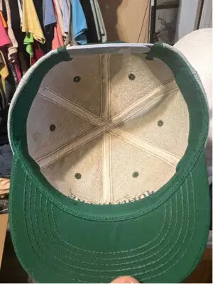 Inside view of a vintage green and beige John Deere hat showing wear and adjustable strap