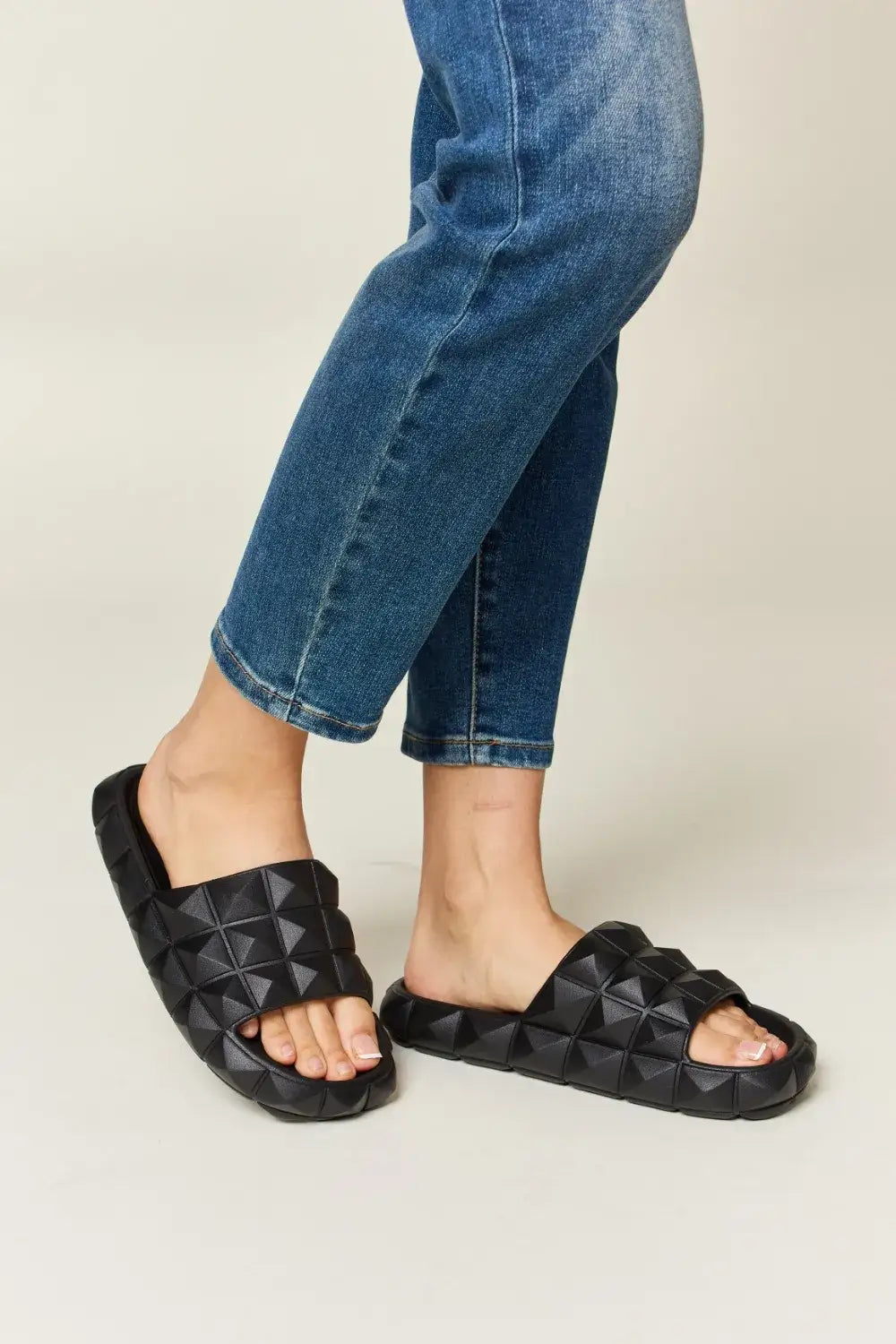Black studded slide sandals with pyramid stud toe band on blue jeans for WILD DIVA Pyramid Stud Toe collection