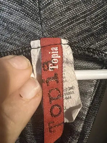 Red fabric clothing tag on gray dress displaying Topia brand and care instructions