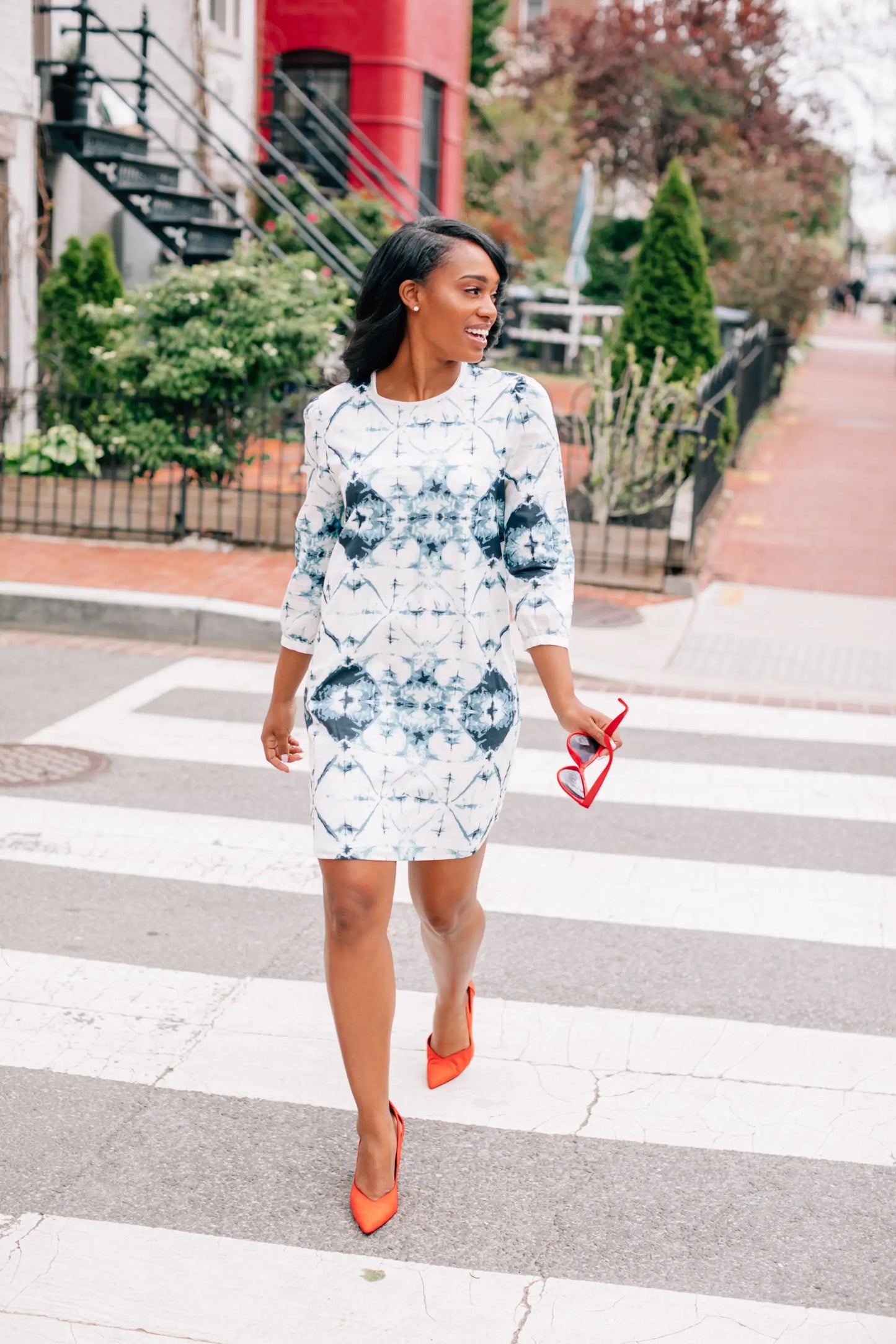 Woman in a white and blue woven slim fit dress holding red heart-shaped sunglasses